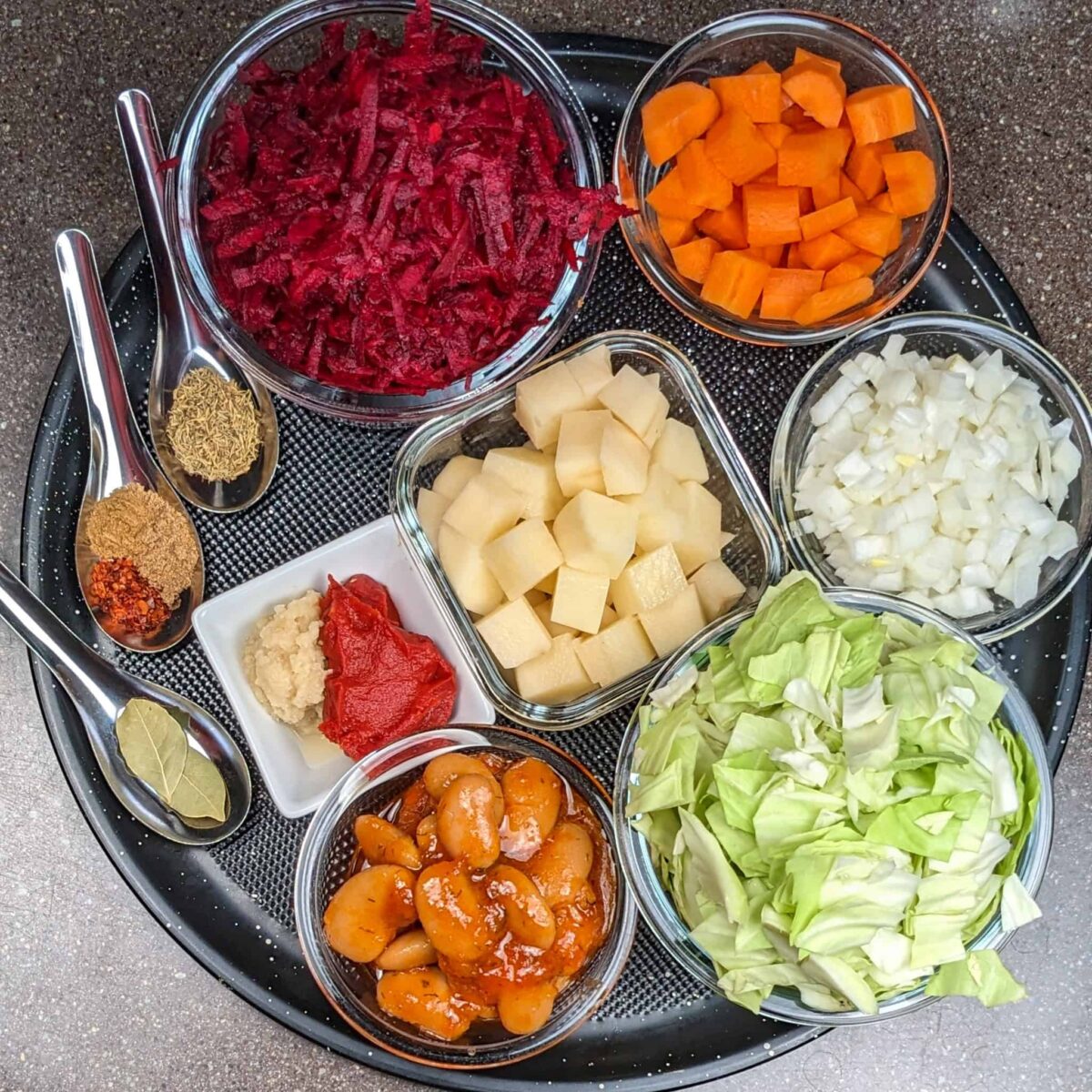 Vibrant vegetable ingredients arranged for a healthy vegetarian borscht recipe on a black tray.